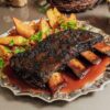 Costela com black rub, assada 14h ao jus, batatas bravas e farofa de cebola brullé